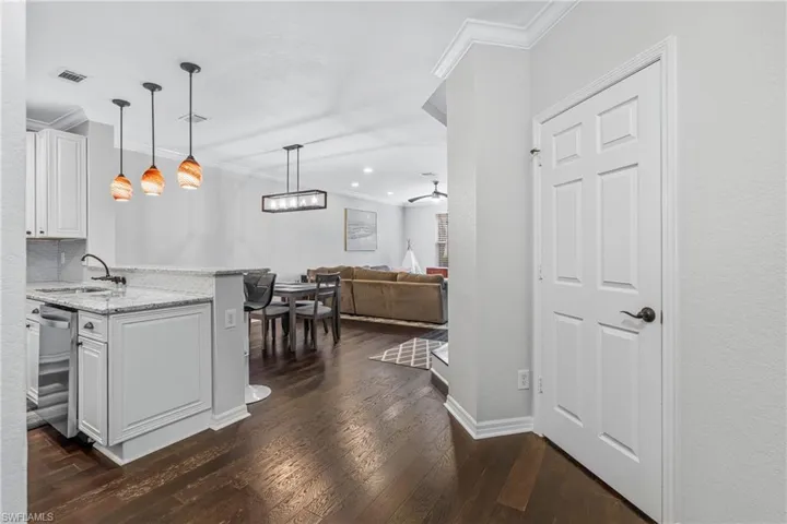 Kitchen with dark wood-type flooring, white cabinetry, decorative light fixtures, dishwasher, and light stone countertops
