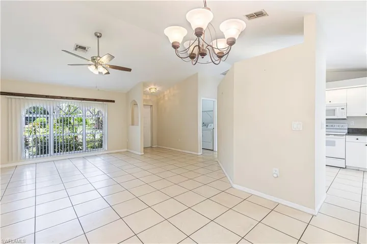 Spare room featuring vaulted ceiling, washer / clothes dryer, a chandelier, light tile patterned flooring, and ceiling fan