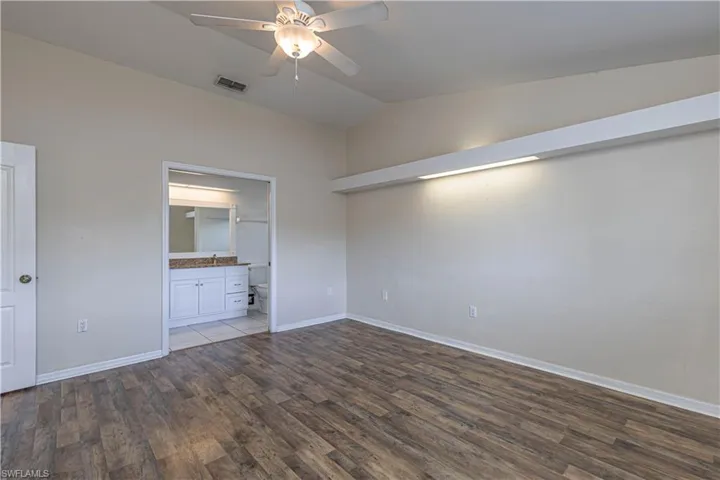 Unfurnished bedroom featuring wood finished floors, vaulted ceiling, ensuite bath, and a ceiling fan