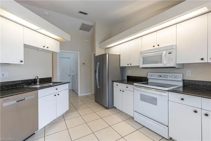 Kitchen with appliances with stainless steel finishes, light tile patterned floors, white cabinets, and dark stone counters