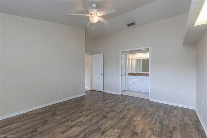Unfurnished bedroom featuring wood finished floors, lofted ceiling, ensuite bathroom, and a ceiling fan