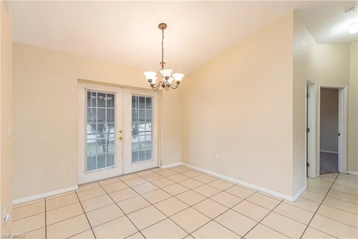 Empty room featuring french doors, light tile patterned floors, and a chandelier