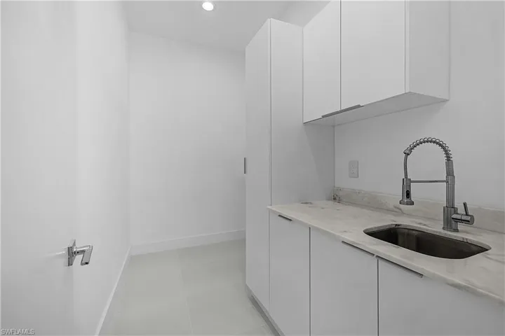 Laundry room featuring white cabinets, light stone countertops, a sink, and light tile patterned floors