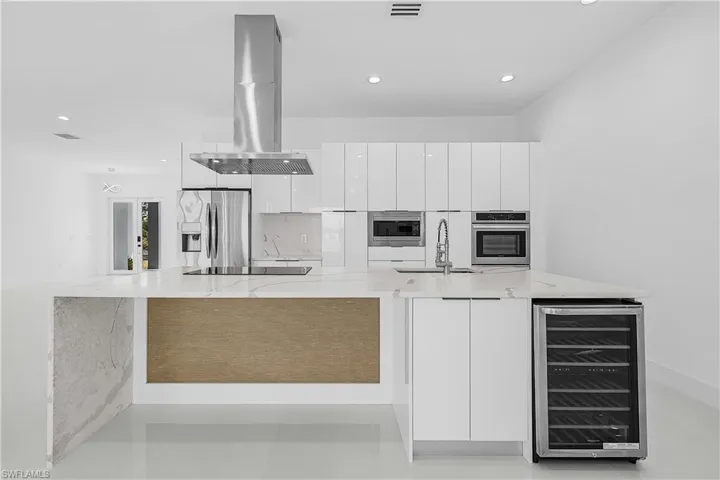 Kitchen featuring island exhaust hood, modern cabinets, stainless steel appliances, a sink, and beverage cooler