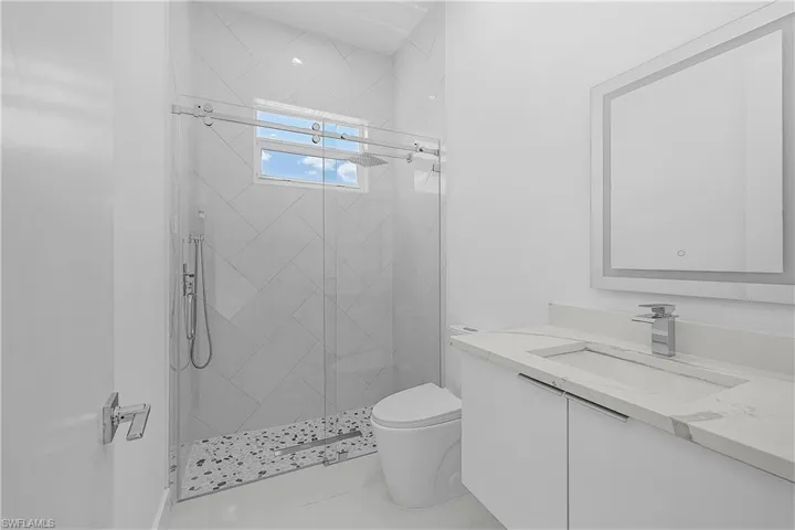 Bathroom featuring toilet, vanity, and a stall shower