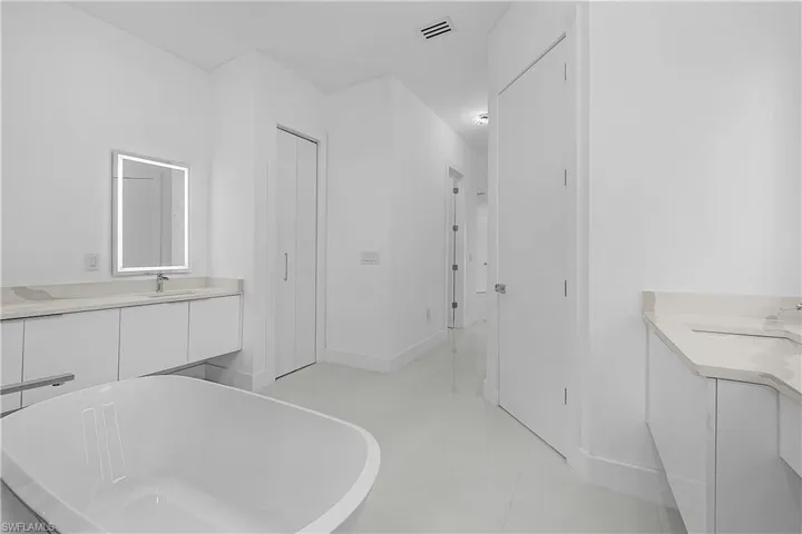 Primary bathroom featuring a soaking tub, a sink, dual vanities, and tile flooring