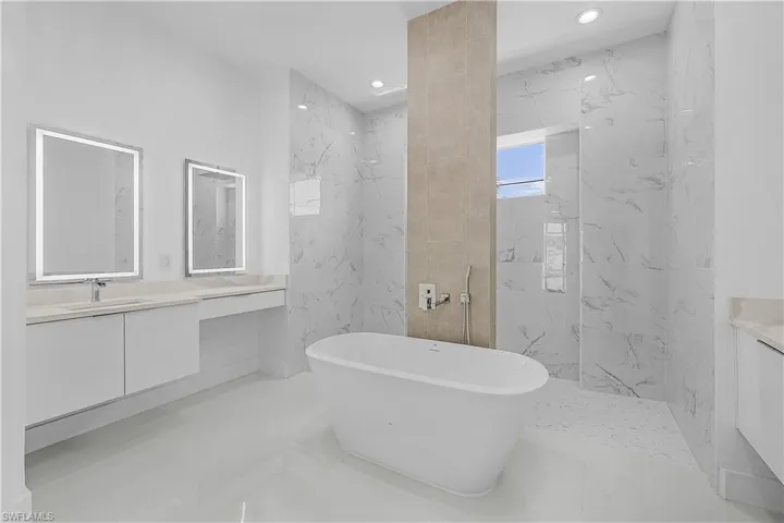 Primary bathroom with tile walls, a freestanding bath, shower, recessed lighting, and vanity
