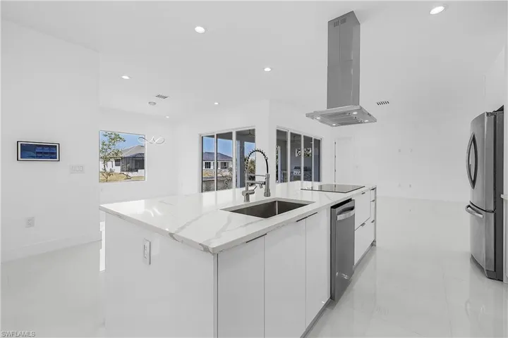 Kitchen with white cabinetry, stainless steel appliances, a sink, modern cabinets, and ventilation hood