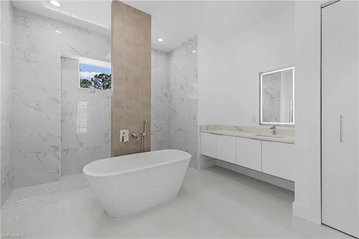 Primary bathroom with a freestanding bath, vanity, and recessed lighting