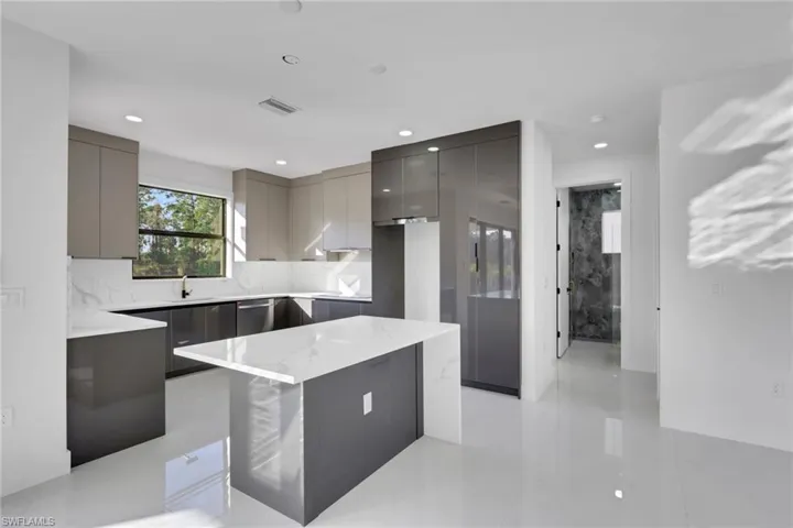 Kitchen with modern cabinets, a center island, gray cabinetry, light stone countertops, and recessed lighting