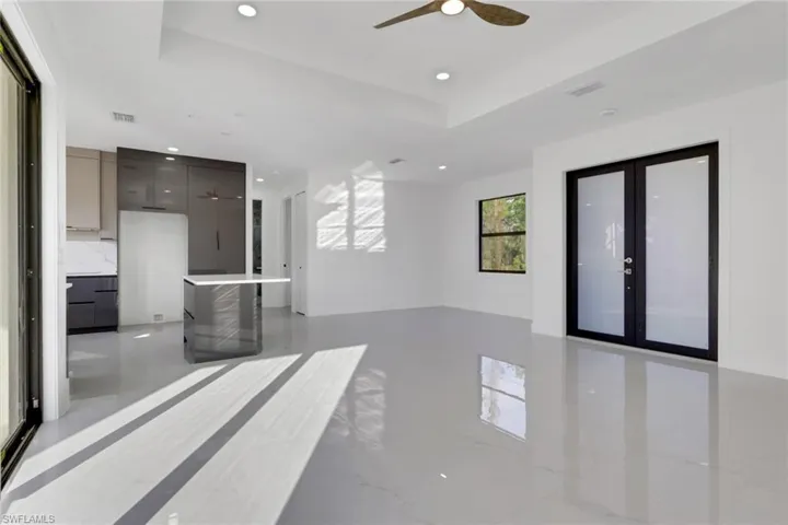 Unfurnished living room with a ceiling fan, a tray ceiling, recessed lighting, light marble finish flooring, and french doors