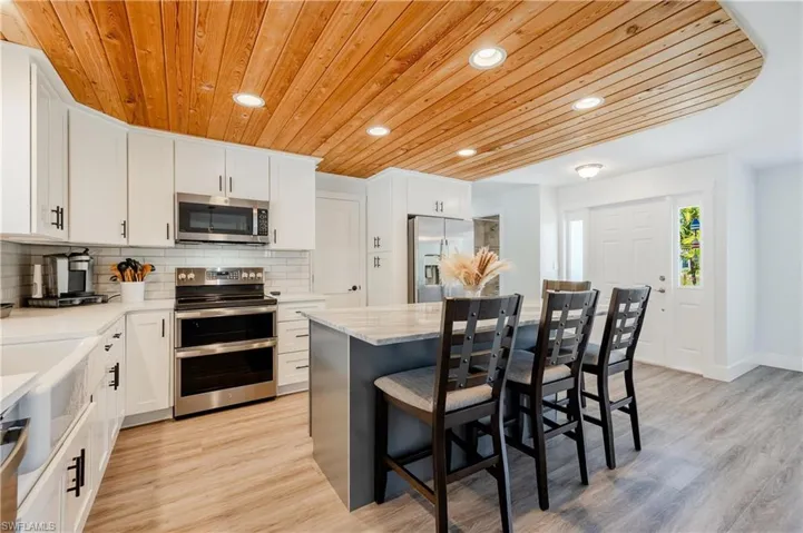 Kitchen featuring light hardwood / wood-style floors, stainless steel appliances, backsplash, a breakfast bar area, and wooden ceiling