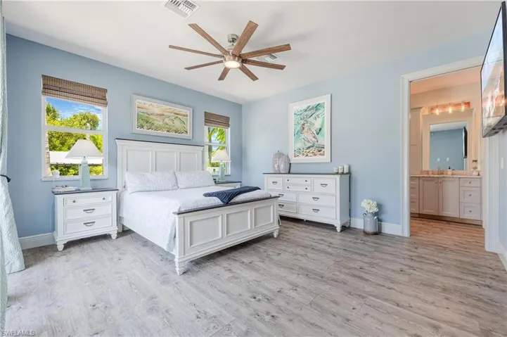 Bedroom with ceiling fan, ensuite bathroom, light hardwood / wood-style flooring, and multiple windows