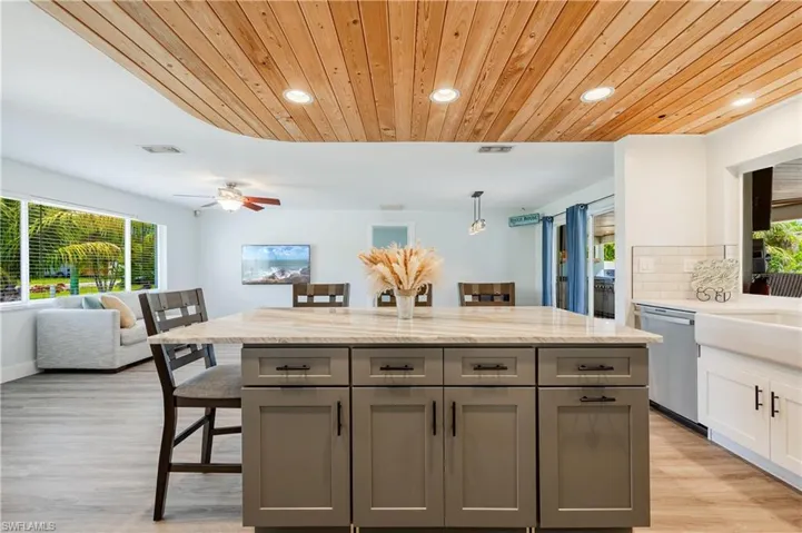 Kitchen featuring ceiling fan, stainless steel dishwasher, light wood-type flooring, a kitchen island, and a kitchen bar