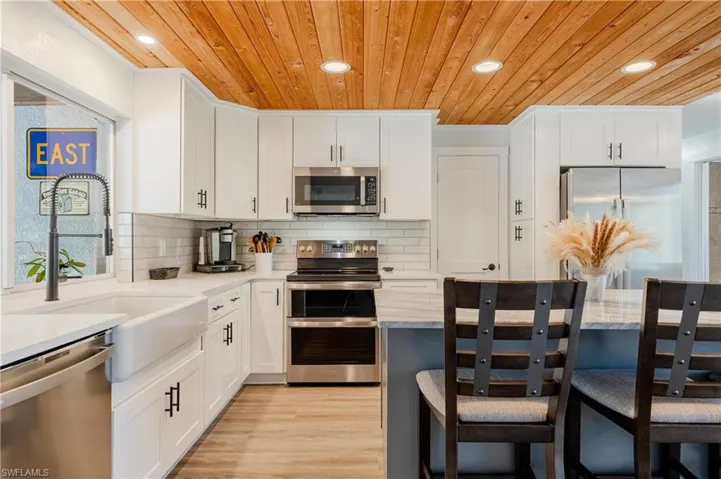 Kitchen with light hardwood / wood-style floors, tasteful backsplash, white cabinetry, and appliances with stainless steel finishes