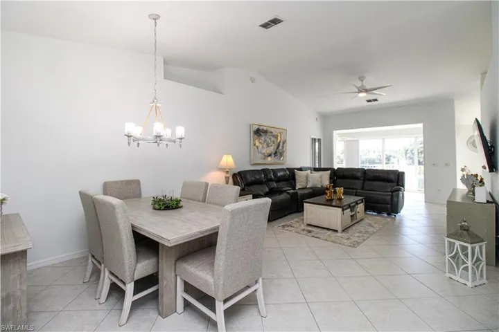 Tiled dining area with ceiling fan with notable chandelier and lofted ceiling