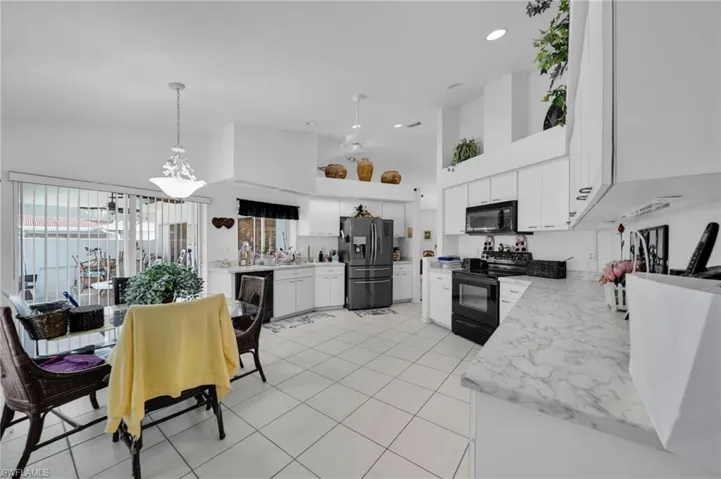 Kitchen with a high ceiling, light countertops, white cabinets, black appliances, and recessed lighting