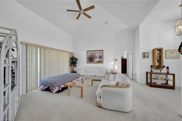 Carpeted living room with ceiling fan and vaulted ceiling