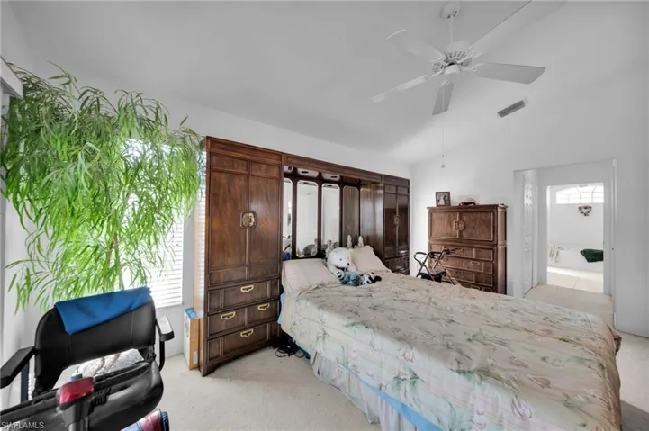 Bedroom featuring light carpet, vaulted ceiling, ceiling fan, and ensuite bath