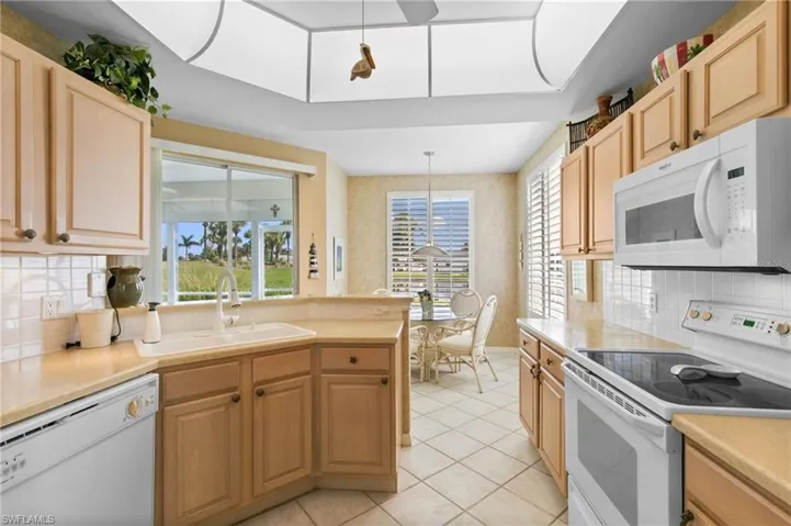 Kitchen featuring light brown cabinetry, pendant lighting, white appliances, sink, and light tile patterned floors