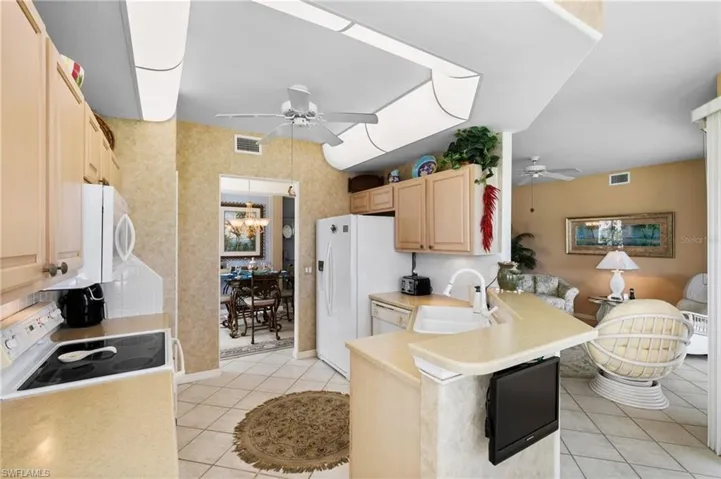 Kitchen featuring light tile patterned floors, ceiling fan with notable chandelier, light brown cabinetry, and kitchen peninsula