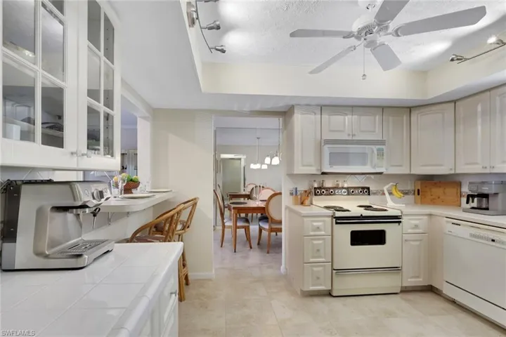 Kitchen featuring white appliances, glass insert cabinets, a raised ceiling, backsplash, and light tile patterned flooring