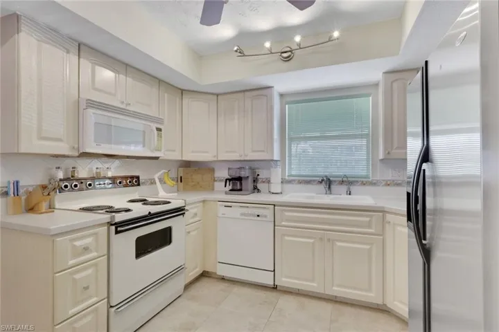 Kitchen featuring white appliances, light countertops, backsplash, and ceiling fan