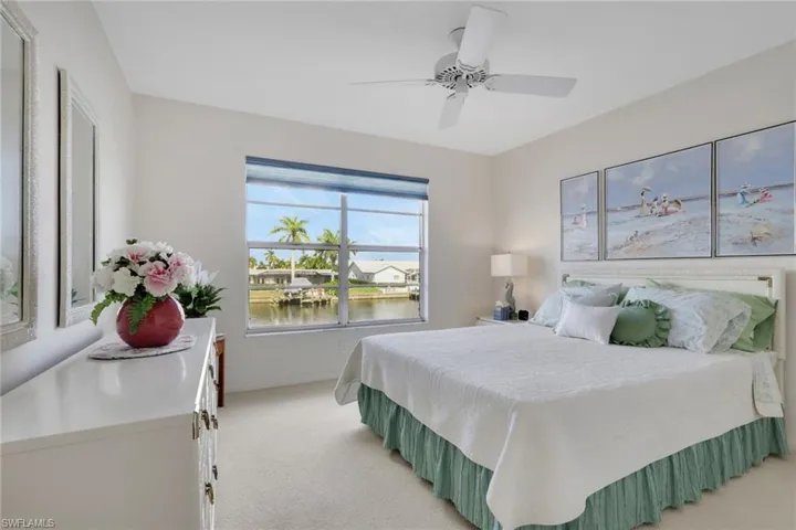 Bedroom with a water view, light colored carpet, and a ceiling fan