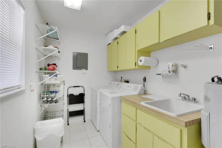 Laundry area with water heater, cabinet space, electric panel, washing machine and dryer, and light tile patterned floors