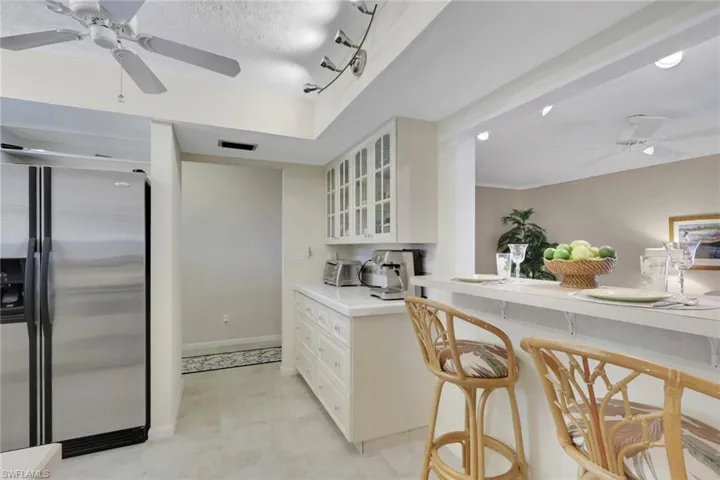 Kitchen with a ceiling fan, stainless steel fridge, light countertops, glass insert cabinets, and a breakfast bar