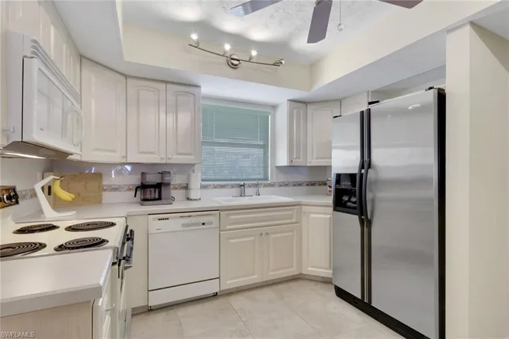 Kitchen with white appliances, light countertops, a tray ceiling, tasteful backsplash, and white cabinetry