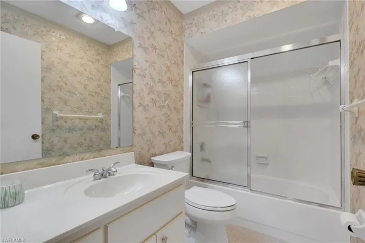 Full bathroom with wallpapered walls, vanity, combined bath / shower with glass door, and crown molding