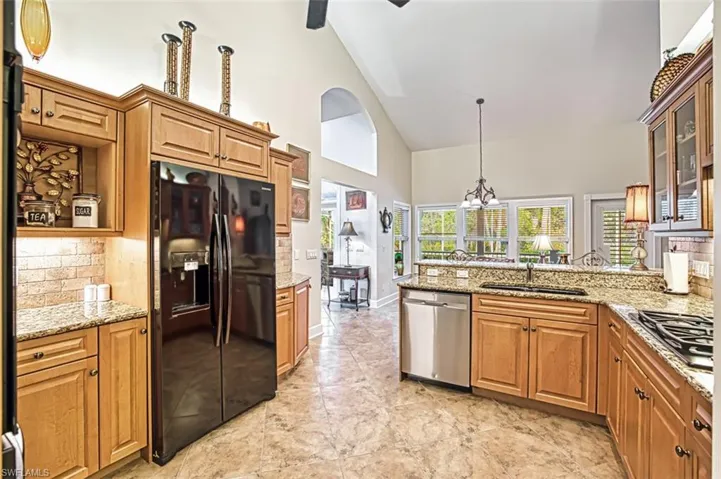 Kitchen with ceiling fan with notable chandelier, hanging light fixtures, high vaulted ceiling, light stone countertops, and appliances with stainless steel finishes