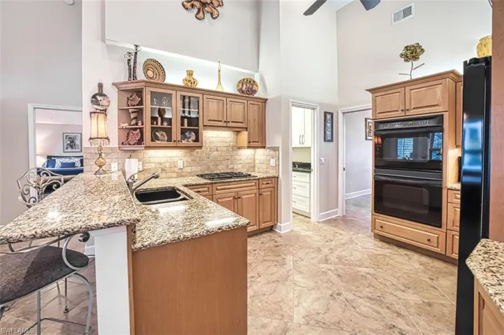 Kitchen featuring black appliances, light stone counters, a towering ceiling, a breakfast bar, and kitchen peninsula
