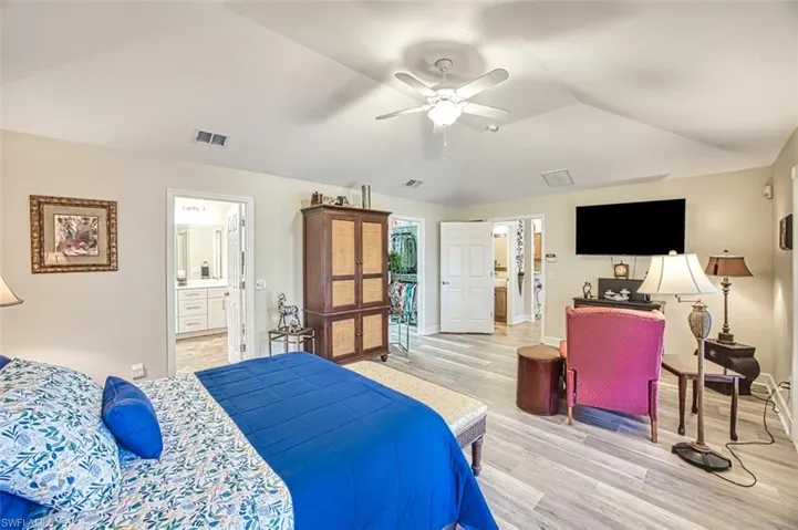 Bedroom featuring ceiling fan, ensuite bath, light hardwood / wood-style flooring, and lofted ceiling