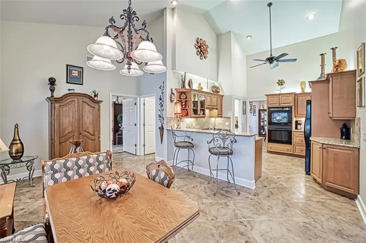 Dining space featuring ceiling fan with notable chandelier and high vaulted ceiling