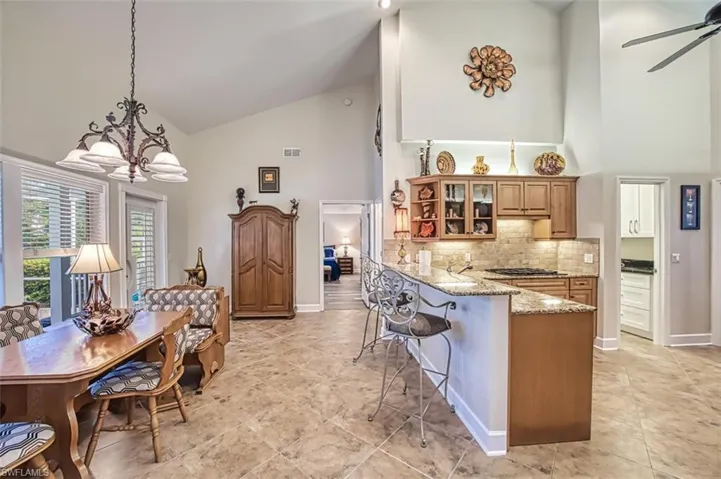 Kitchen featuring kitchen peninsula, light stone countertops, a breakfast bar area, high vaulted ceiling, and pendant lighting