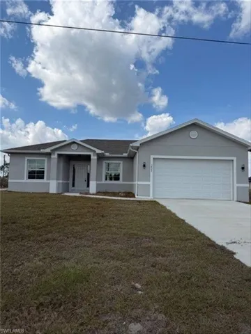 Ranch-style house featuring a front lawn, stucco siding, an attached garage, and driveway