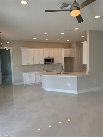 Kitchen featuring white cabinets, ceiling fan, stainless steel microwave, a peninsula, and recessed lighting