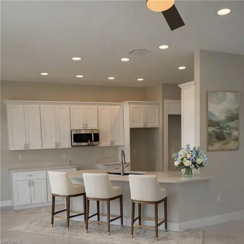 Kitchen featuring a kitchen bar, a peninsula, white cabinets, recessed lighting, and stainless steel microwave