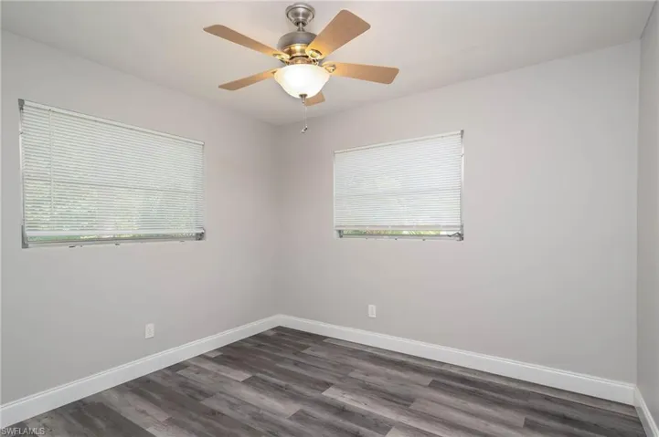 Empty room with dark wood-style flooring, healthy amount of natural light, and a ceiling fan