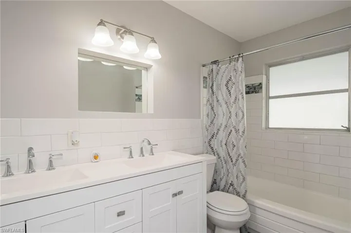 Full bath with tile walls, double vanity, and shower / bath combo with shower curtain