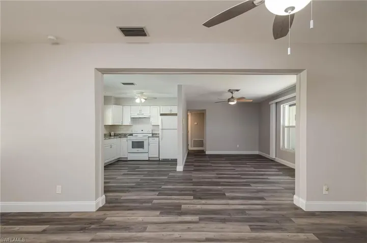 Unfurnished living room featuring ceiling fan and dark wood-style floors