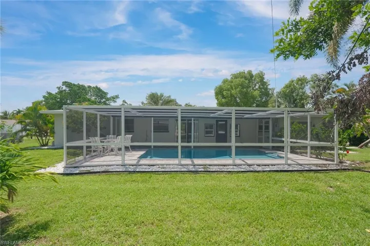 Rear view of property featuring a yard, an outdoor pool, glass enclosure, and a patio area