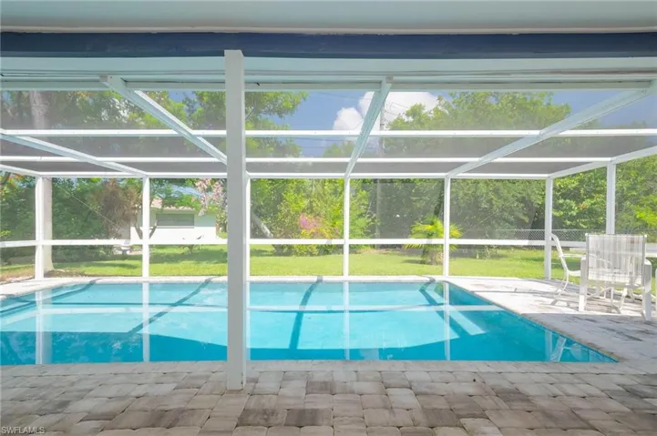 Swimming pool with a patio, glass enclosure, and a yard