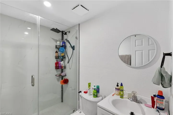 Glass-enclosed shower with white tiled walls and a black rainfall showerhead