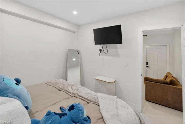 Recessed lighting illuminates a bright interior with white walls, a wall-mounted television, and a white paneled door