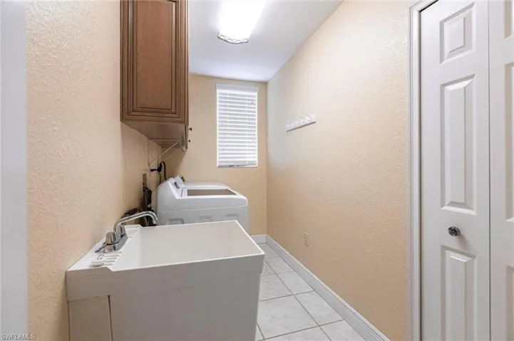 Laundry area featuring a textured wall, cabinet space, light tile patterned floors, and washing machine and clothes dryer
