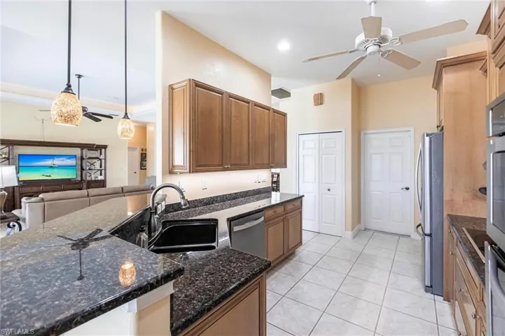 Kitchen with a ceiling fan, light tile patterned flooring, dark stone countertops, open floor plan, and brown cabinetry