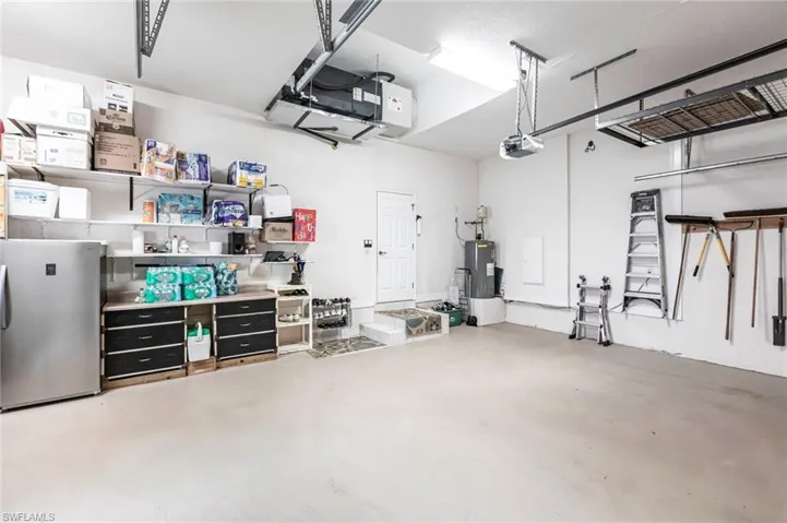 Garage featuring freestanding refrigerator, water heater, and a garage door opener